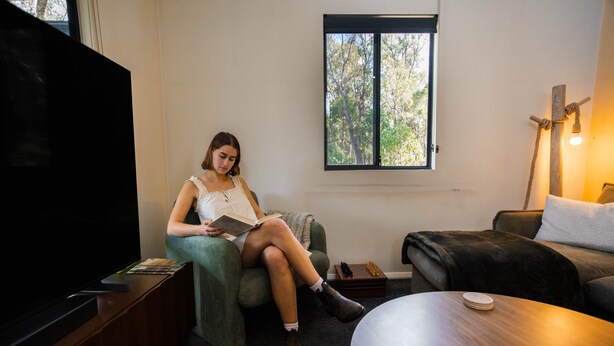 A room with a television, a window with a view of trees, a sofa, a small table, and a lamp.