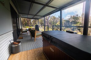 Un espacio de estar al aire libre techado con jacuzzi, terraza de madera y vistas a árboles.