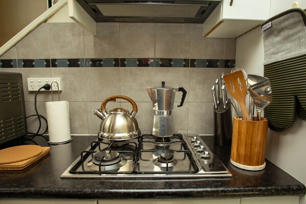 A kitchen with a gas stove, kettle, and various utensils.