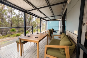 Un espacio al aire libre techado con piso de madera, una mesa con sillas y un sofá.