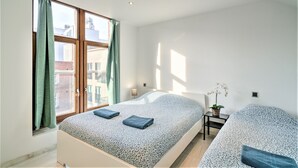 A modern bedroom with a large window, a bed with a patterned bedspread, a bedside table with a lamp, and a small potted plant. - 9-persons apartment in centre of Antwerp (belgium)