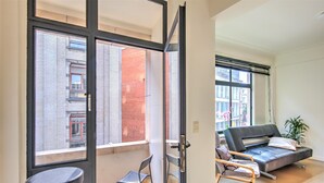 A modern apartment with a balcony, a sofa, a chair, and a small table. - Spacious apartment in heart of Antwerp (Antwerp Center)