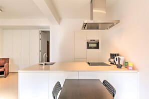 A modern kitchen with a central island, built-in oven, and stainless steel range hood. - Spacious apartment in heart of Antwerp (Antwerp Center)