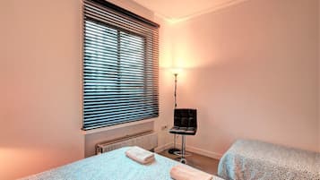 A bedroom with a bed, a radiator, a standing lamp, and a window with blinds.
