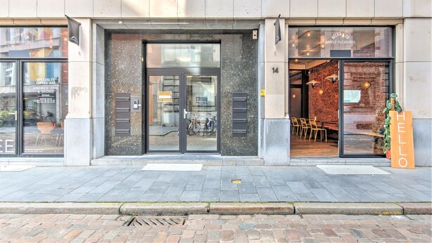 A building with a glass door entrance, a sign reading 'HELLO,' and a brick wall interior visible through the window. - Spacious apartment in heart of Antwerp (Antwerp Center)