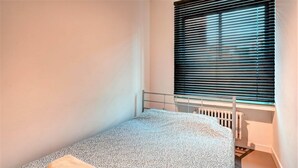 A small, single-bed room with a radiator, a window with blinds, and a towel on the bed. - Spacious apartment in heart of Antwerp (Antwerp Center)