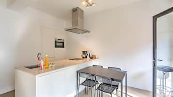 A modern kitchen with a central island, a dining table with chairs, and a built-in oven.