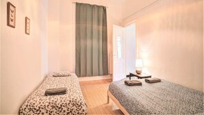 Una habitación con dos camas individuales, una ventana con cortinas, una lámpara en una mesita de noche y cuadros enmarcados en la pared.