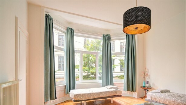 Una habitación con dos camas, una ventana con cortinas, una lámpara colgante y una pequeña mesa con un florero.