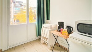Una habitación con puerta de vidrio corredera, una mesa con tetera, cafetera y microondas. Hay sillas de plástico blanco apiladas junto a la pared.