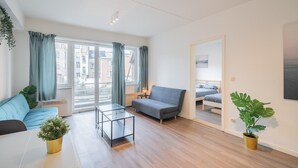 A modern living room with a sofa, a glass coffee table, and a bed in the adjacent room. - Antwerp bright apartment stay (Antwerp)