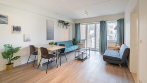 A modern living room with a sofa, a dining table with chairs, a small coffee table, and a potted plant. - Antwerp bright apartment stay (Antwerp)