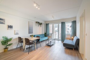 Een moderne woonkamer met een bank, een eettafel met stoelen, een klein bijzettafeltje en een potplant.