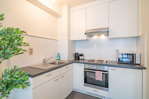 A compact kitchen with white cabinets, a stainless steel sink, a microwave, and a built-in oven. - Stay in the heart of Antwerp (Antwerp)