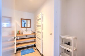 Ein Badezimmer mit einem weißen Waschbecken, einem Spiegel und Regalen.