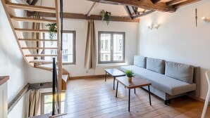 Un appartement de style « loft » avec des poutres apparentes, un escalier, un canapé, une petite table et une plante suspendue.
