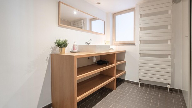 Une salle de bain avec un meuble-lavabo en bois, un miroir, un évier, une plante en pot et un radiateur.
