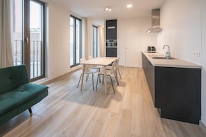 Et moderne køkken med en central ø, et spiseområde med bord og stole, samt en grøn sofa.