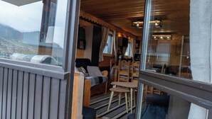 A cozy cabin interior with a wooden ceiling, a sofa, a dining table, and a view through a large window. - Chez Jerome I T3 I Châtel (Châtel)