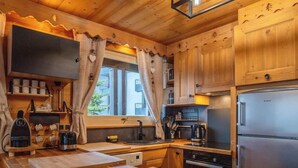 A wooden kitchen with a built-in oven, a stainless steel refrigerator, and a window with curtains. - Chez Jerome I T3 I Châtel (Châtel)