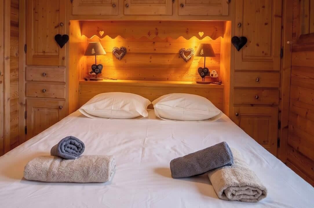 A wooden room with a bed, two heart-shaped wall decorations, and two bedside lamps.