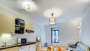 A compact kitchen with a microwave, toaster, and coffee maker. There is a dining table with chairs and a sofa with floral upholstery. A window provides natural light. - Duplex Apartment in the Heart of Luchon (Bagneres-de-Luchon)