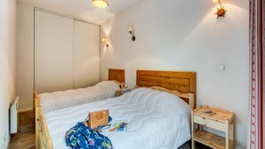 A bedroom with a wooden bed, a nightstand, a wall-mounted lamp, and a door. - Duplex Apartment in the Heart of Luchon (Bagneres-de-Luchon)