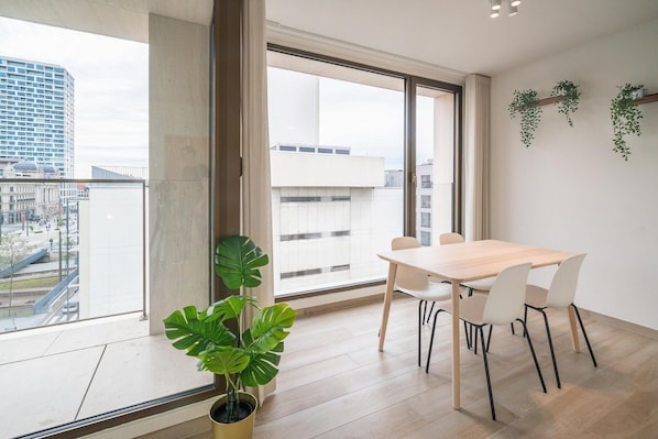 Ein modernes Zimmer mit großem Fenster, einem Esstisch, Stühlen und einem Blumentopf.