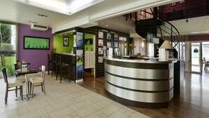 A modern hotel lobby with a curved reception desk, a staircase, and a dining area with chairs and a table. - Spacious Stay for 6 in La Rochelle (Lagord)