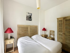 A bedroom with a bed, two bedside tables with lamps, a wooden headboard, a small chair, and a wardrobe. - Spacious Stay for 6 in La Rochelle (Lagord)