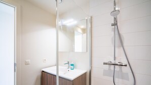 Een moderne badkamer met een douchecabine van glas, een witte wastafel en een spiegel.