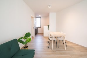 Un apartamento moderno con un sofá verde, una mesa de comedor con sillas y una planta en maceta.