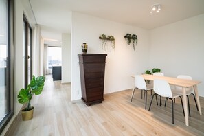 A modern room with a wooden floor, a dining table with chairs, a tall cabinet, and potted plants. - Executive 3BR Apartment in Antwerp (Antwerp)