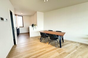 A modern dining area with a wooden table and black chairs, a small plant on a white cabinet, and a wooden floor. - Spacious City Retreat with Balcony (Antwerp)