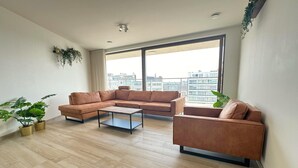 A modern living room with a sectional sofa, a coffee table, and potted plants. - Spacious City Retreat with Balcony (Antwerp)