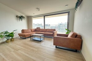 A modern living room with a sectional sofa, a coffee table, and potted plants. - Spacious City Retreat with Balcony (Antwerp)