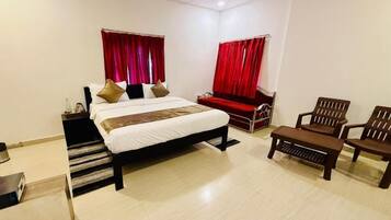 A hotel room with a bed, two chairs, a small table, and a ceiling fan.