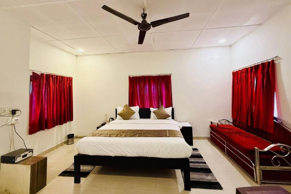 Un dormitorio con cama, ventilador de techo, cortinas rojas y una mesita de noche.