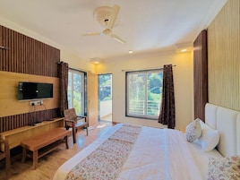 Un dormitorio con cama, televisor, banco, ventilador de techo y ventanas grandes.