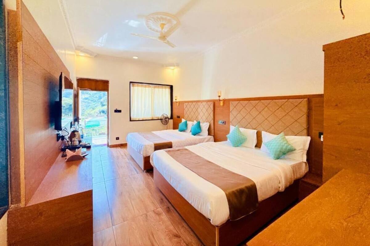 Una habitación de hotel con dos camas, ventilador de techo, televisión y ventana con cortinas.