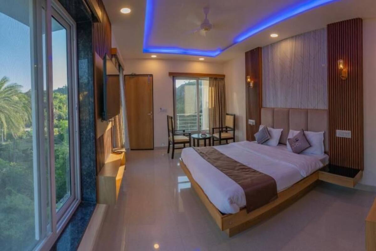 Habitación de hotel moderna con una cama grande, un balcón, zona de comedor y vistas al exterior.