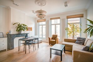 Ein modernes Wohnzimmer mit einer Couch, einem Esstisch, Stühlen, einem Kamin und großen Fenstern.