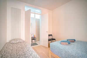 Ein Schlafzimmer mit zwei Betten, einem Sessel, einer Heizung und einem durch eine offene Tür einsehbaren Badezimmer.
