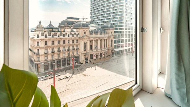 Vista desde una ventana sobre una plaza con edificios históricos y un rascacielos moderno.
