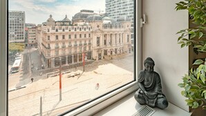 Una habitación con un amplio ventanal con vistas a un paisaje urbano, una estatua de Buda y una planta en maceta.