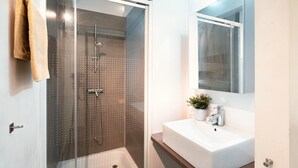 Un baño moderno con ducha acristalada, un lavabo blanco y un espejo encima.