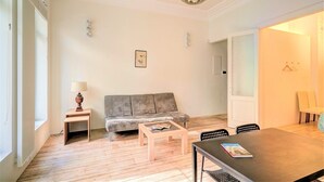 A living room with a sofa, a coffee table, a dining table, and a lamp. - 2-bedroom apartment in Antwerp Centre (Antwerp)