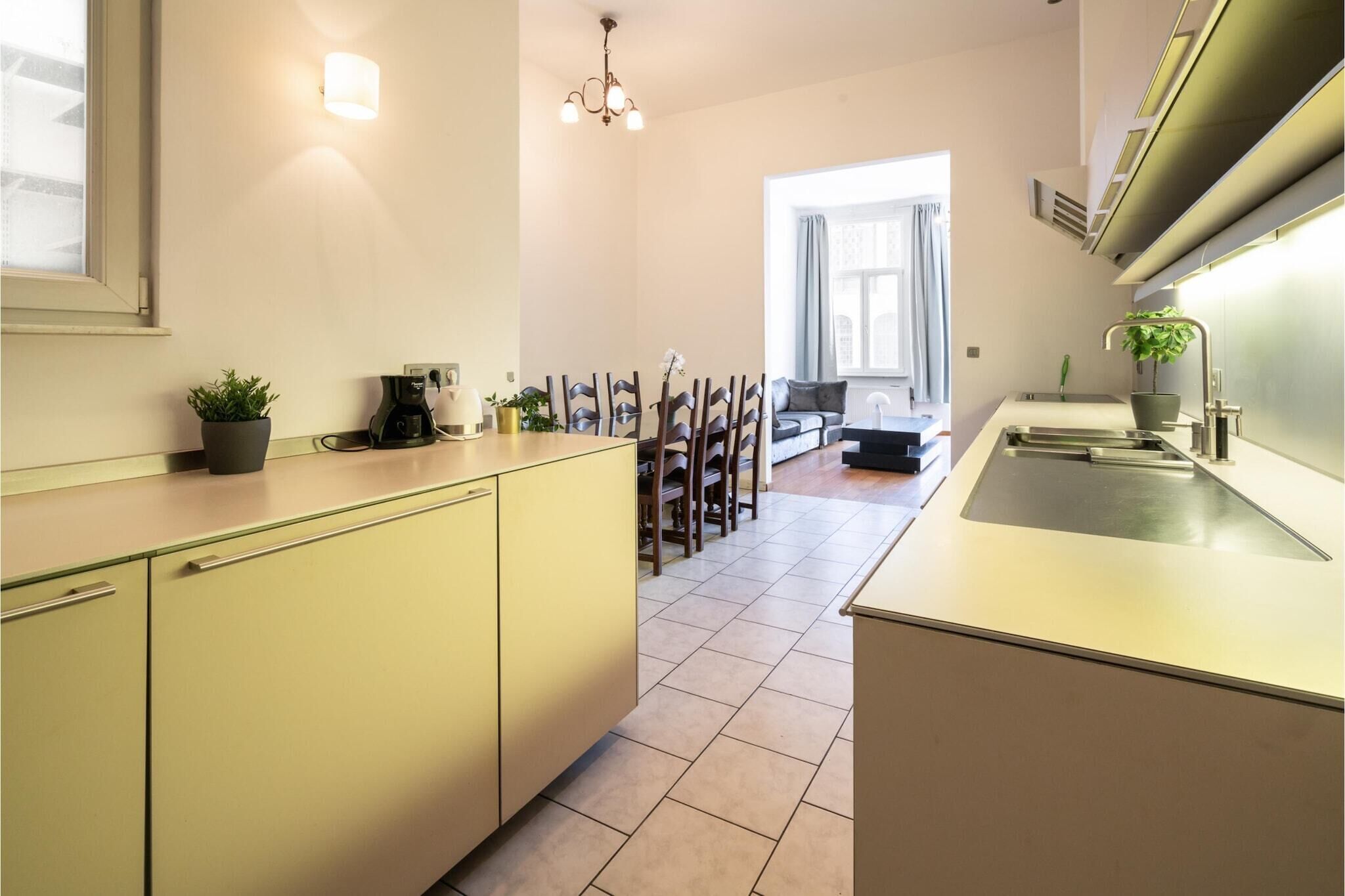 A modern kitchen with a dining area, featuring a coffee maker, a sink, and a potted plant.