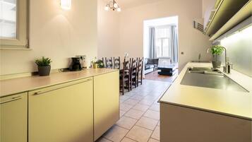 A modern kitchen with a dining area, featuring a coffee maker, a sink, and a potted plant.