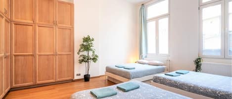 A bedroom with two beds, wooden wardrobes, a potted plant, and a window with curtains.